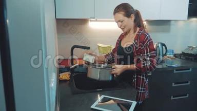 女孩在厨房的砧板上洗碗，看着一台数字平板电脑。 女人在厨房做饭。 女孩洗了一个